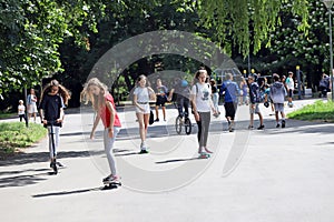 Kids or children are having fun in the park in summertime, skateboarding, riding bikes