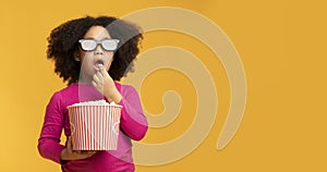 Kids cinema. Black little girl wearing 3D glasses and eating popcorn