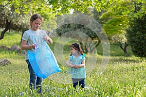 Kids cleaning in park.Volunteer children with a garbage bag cleaning up litter, putting plastic bottle in recycling bag.