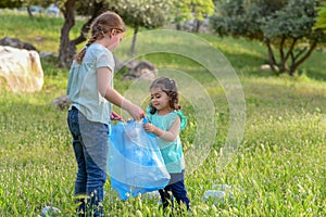 Kids cleaning in park.Volunteer children with a garbage bag cleaning up litter, putting plastic bottle in recycling bag.