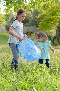 Kids cleaning in park.Volunteer children with a garbage bag cleaning up litter, putting plastic bottle in recycling bag.