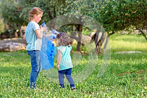 Kids cleaning in park.Volunteer children with a garbage bag cleaning up litter, putting plastic bottle in recycling bag.