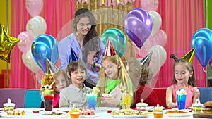 Kids in colorful hats celebrating birthday with mother and fiends.