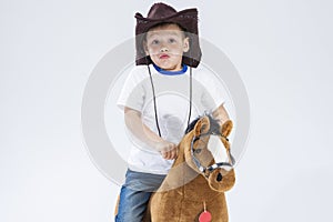 Kids Consepts. Portrait of Caucasian Little Boy in Cowboy Clothing Making Fases Posing With Symbolic Plush Horse Against White. photo
