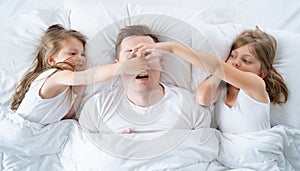 Kids, dad sleep together in bed. Father is snoring hard, girls, daughters pinch nose with fingers. Disorders, joint sleeping.