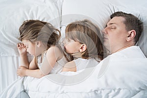 Kids, dad sleep together in bed on pillows under blanket. Family joint sleeping. Father with cute little daughters. Insomnia,