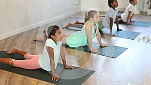 Kids doing bhudjangasana exercise laying on yoga mats in gym.