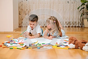 Kids drawing on floor on paper. Preschool boy and girl play on floor with educational toys - blocks, train, railroad