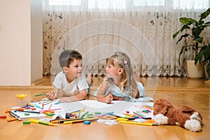 Kids drawing on floor on paper. Preschool boy and girl play on floor with educational toys - blocks, train, railroad