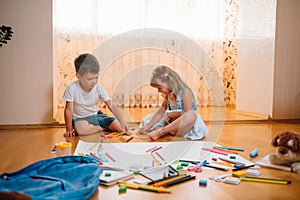 Kids drawing on floor on paper. Preschool boy and girl play on floor with educational toys - blocks, train, railroad