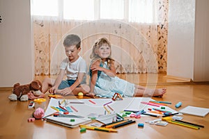 Kids drawing on floor on paper. Preschool boy and girl play on floor with educational toys - blocks, train, railroad