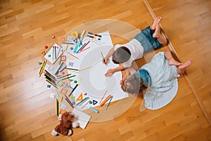 Kids drawing on floor on paper. Preschool boy and girl play on floor with educational toys - blocks, train, railroad, plane. Toys