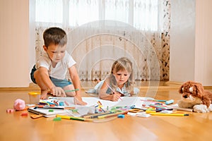 Kids drawing on floor on paper. Preschool boy and girl play on floor with educational toys - blocks, train, railroad, plane. Toys