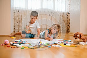 Kids drawing on floor on paper. Preschool boy and girl play on floor with educational toys - blocks, train, railroad, plane. Toys