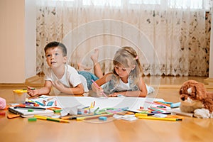 Kids drawing on floor on paper. Preschool boy and girl play on floor with educational toys - blocks, train, railroad, plane. Toys