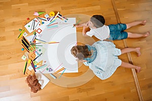 Kids drawing on floor on paper. Preschool boy and girl play on floor with educational toys - blocks, train, railroad, plane. Toys