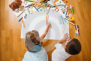 Kids drawing on floor on paper. Preschool boy and girl play on floor with educational toys - blocks, train, railroad, plane. Toys