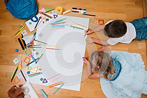 Kids drawing on floor on paper. Preschool boy and girl play on floor with educational toys - blocks, train, railroad, plane. Toys