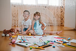 Kids drawing on floor on paper. Preschool boy and girl play on floor with educational toys - blocks, train, railroad, plane. Toys