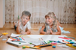 Kids drawing on floor on paper. Preschool boy and girl play on floor with educational toys - blocks, train, railroad, plane. Toys