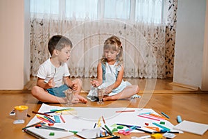 Kids drawing on floor on paper. Preschool boy and girl play on floor with educational toys - blocks, train, railroad, plane. Toys