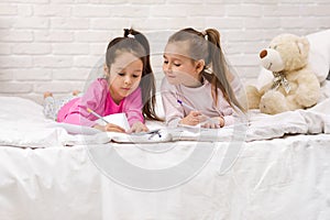 Kids drawing pictures while lying on bed.