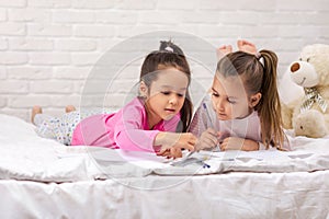 Kids drawing pictures while lying on bed.