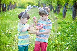 Kids on Easter egg hunt in blooming spring garden. Children searching for colorful eggs in flower meadow. Toddler boy and his brot