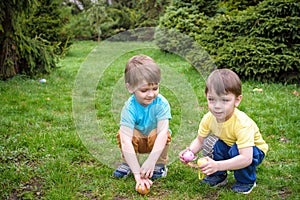 Kids on Easter egg hunt in blooming spring garden. Children searching for colorful eggs in flower meadow. Toddler boy and his brot