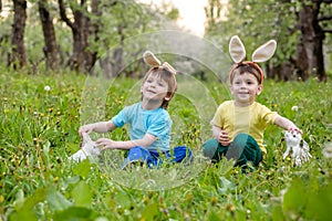 Kids on Easter egg hunt in blooming spring garden. Children searching for colorful eggs in flower meadow. Toddler boy and his brot