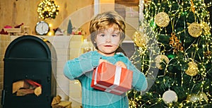 Kids enjoy the holiday. Christmas child holding a red gift box. Happy little boy child with present or gift box indoors.