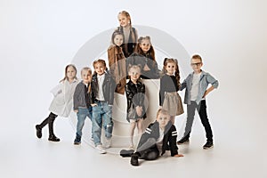 Group of happy smiling kids, little girls and boys in modern outfits posing on grey studio background. Beauty, kids