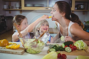 Kids feeding a slice of yellow bell pepper to mother in kitchen