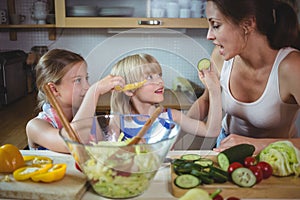 Kids feeding a slice of zucchini to mother in kitchen