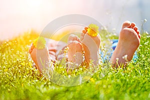 Kids feet with dandelion flowers lying on green grass in sunny