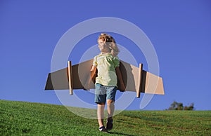 Kids fly. Funny child boy pilot flying with toy cardboard airplane wings on blue sky, copy space. Start up freedom