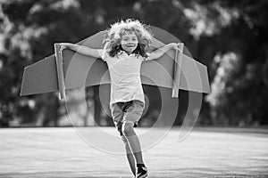 Kids fly. Funny child boy pilot flying with toy cardboard airplane wings in park, copy space. Start up freedom concept