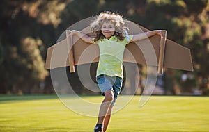 Kids fly. Funny child boy pilot flying with toy cardboard airplane wings in park, copy space. Start up freedom concept
