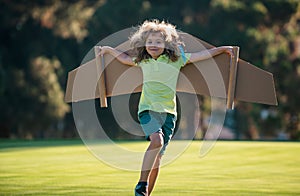 Kids fly. Funny child boy pilot flying with toy cardboard airplane wings in park, copy space. Start up freedom concept