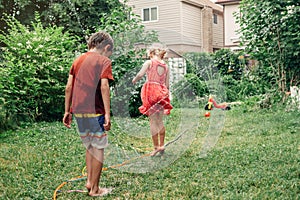 Kids friends splashing with gardening hose sprinkler on backyard on summer day.