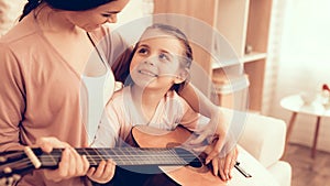 Mom with Guitar in Hand and Girl Sitting on Carpet