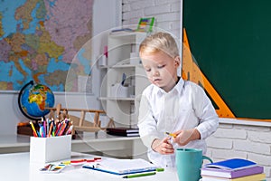 Kids gets ready for school. School interiors.Happy cute industrious child is sitting at a desk indoors.