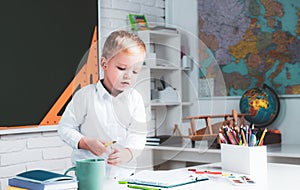 Kids gets ready for school. School interiors.Happy cute industrious child is sitting at a desk indoors.