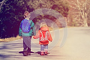 Kids go to school - brother and sister with backpacks walking on the road