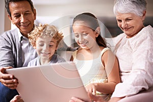 Kids with grandparents. A shot of two kids and their grandparents using a digital tablet while sitting on the sofa.