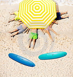 Kids group under umbrella on sand with surfboards