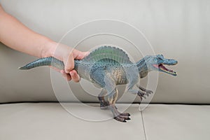 Kids hand catching a greu spinosaurus toy on a sofa