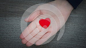 Kids hand holding a heart over wooden background in a conceptual image of love, family and care