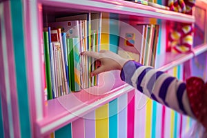 kids hand pulling a book from a candystriped shelf