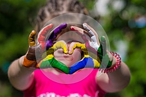 Kids hands in color paints make a heart shape, focus on hands